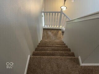 Carpeted staircase with white baluster railing and wall-mounted lighting fixture