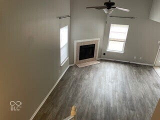 Vaulted ceiling with a ceiling fan, wood-finish flooring, and a fireplace with a tile surround and hearth
