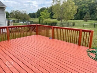 Expansive red-stained deck with matching railings, overlooking a fenced yard and natural water feature with surrounding greenery