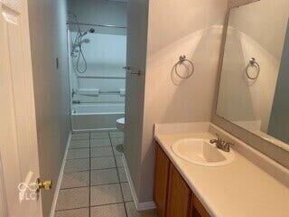 Bathroom featuring a vanity with a counter-mounted sink, a large wall-mounted mirror, wood-finish cabinetry, tile flooring, and a shower/tub combination