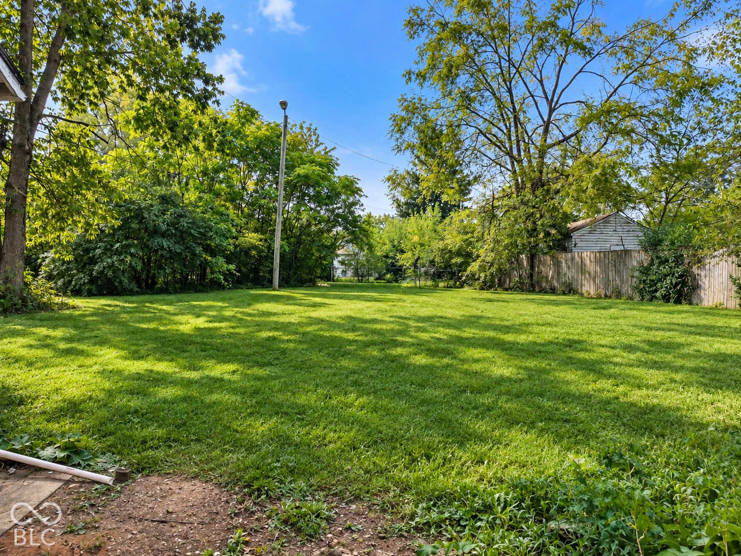 Expansive grassy lot bordered by mature trees and a wood fence
