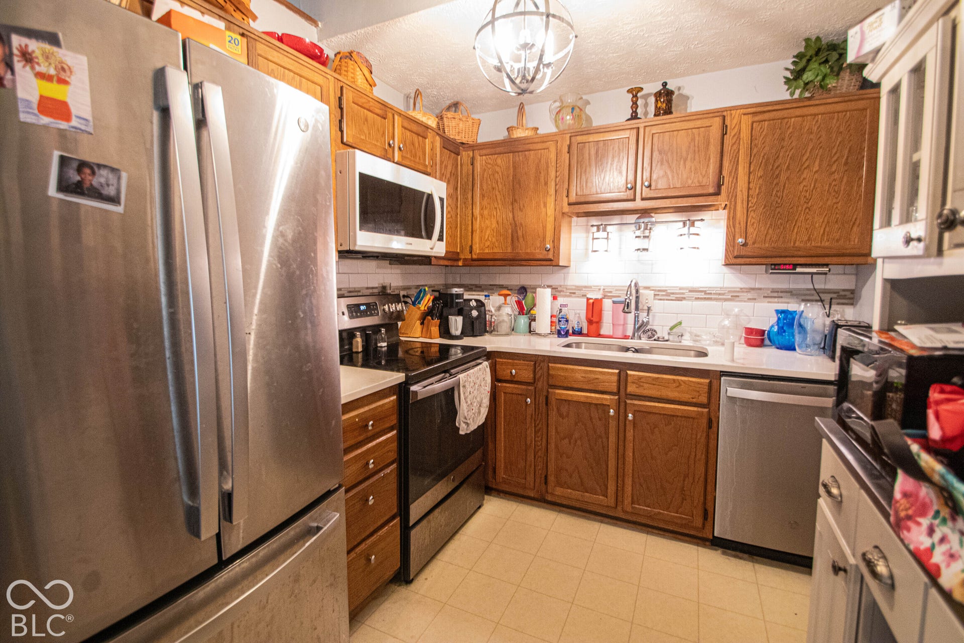 Wood-finish cabinetry, stainless steel appliances, white subway tile backsplash, and light-toned countertops