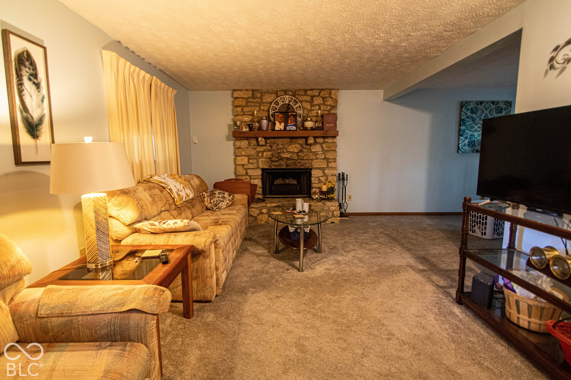 Stone-clad fireplace with a wood mantle, neutral carpeting, and a built-in entertainment unit