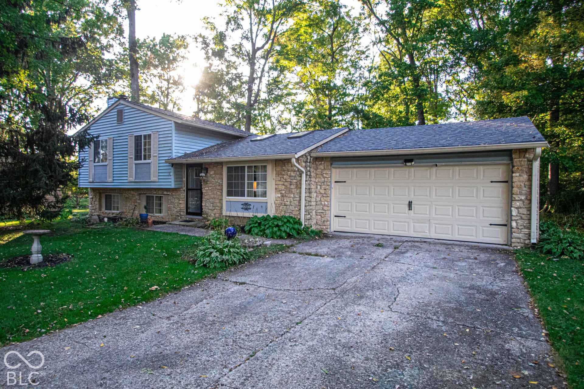 Exterior featuring a stone facade, light blue siding, a multi-pane garage door, and mature trees
