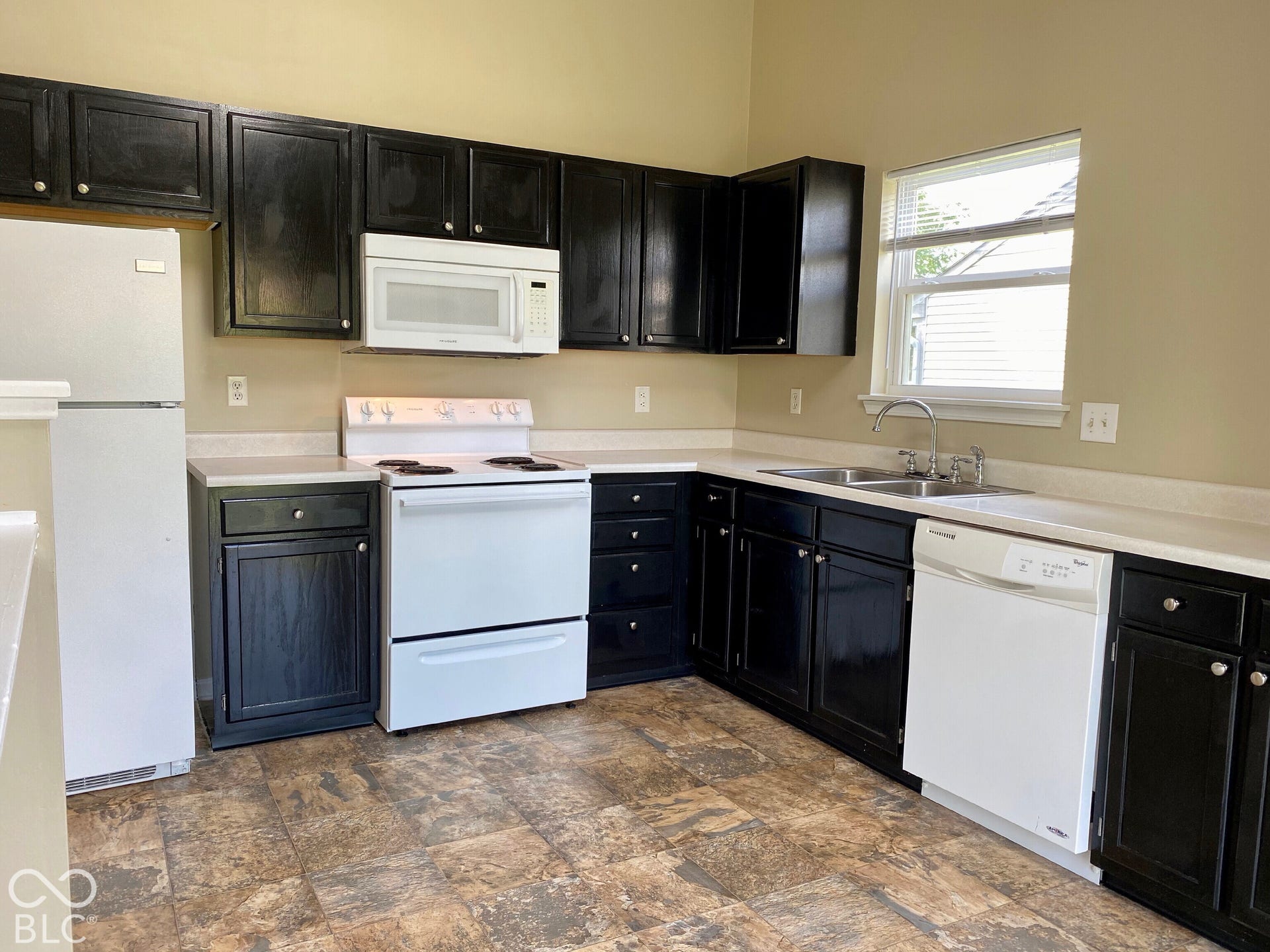3911 Bonn Drive, Indianapolis, IN 46228 Kitchen featuring dark wood-finish cabinetry, white appliances, a double basin sink, and a window with blinds