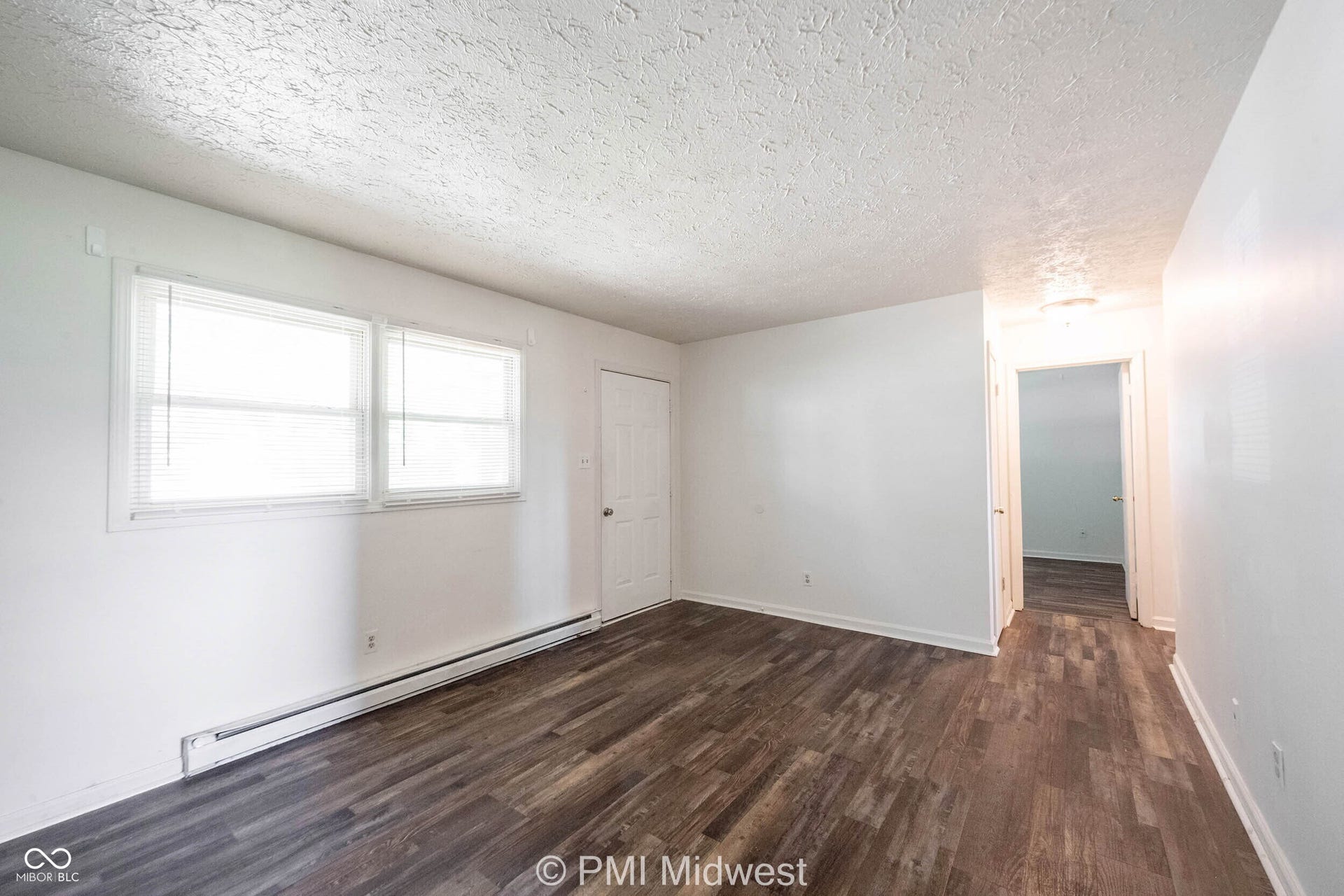 Spacious room featuring wood-finish flooring, white walls, and a textured ceiling