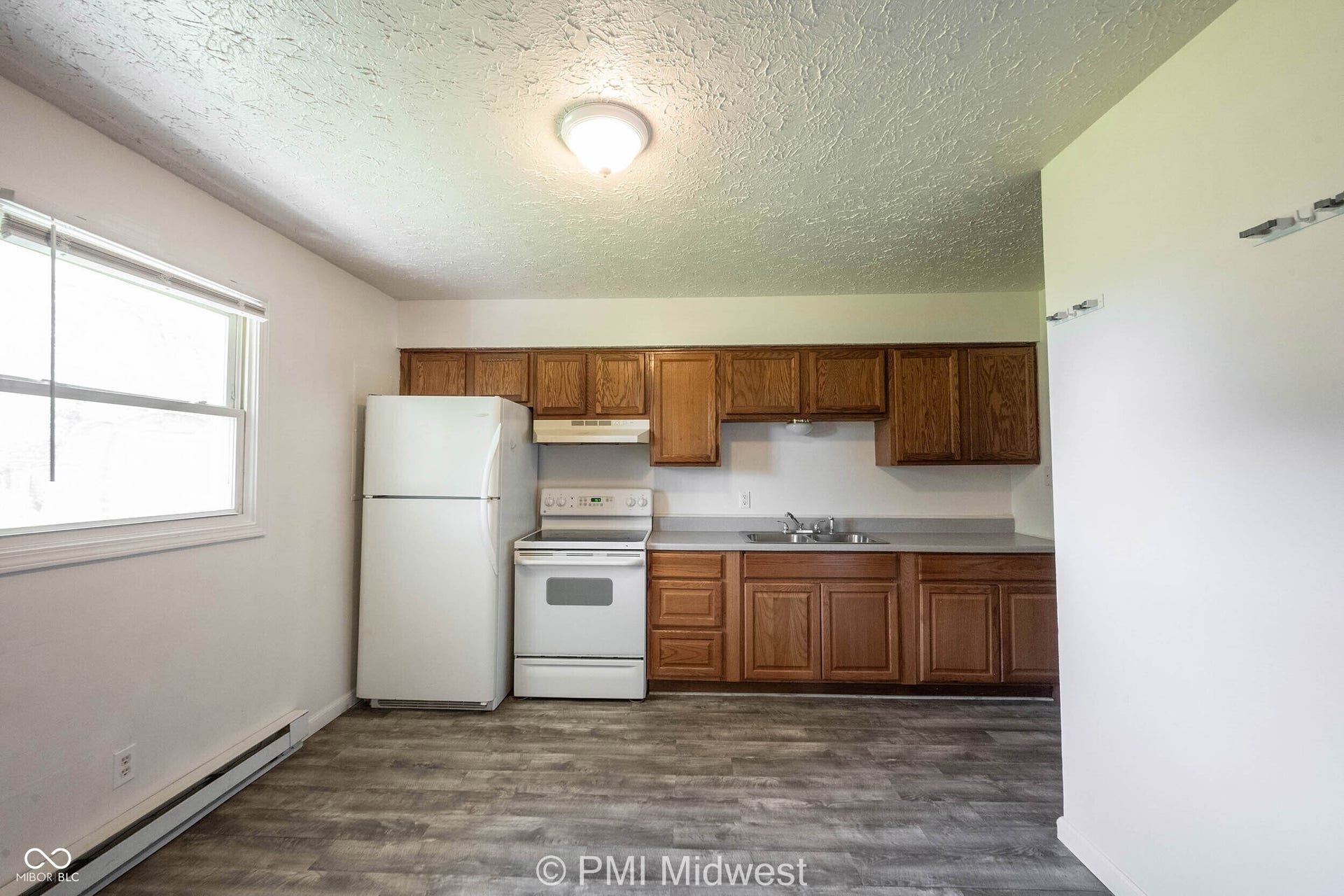 Kitchen area featuring wood-finish flooring, wood cabinetry, light countertops, and a full suite of white appliances including a refrigerator, range, and range hood