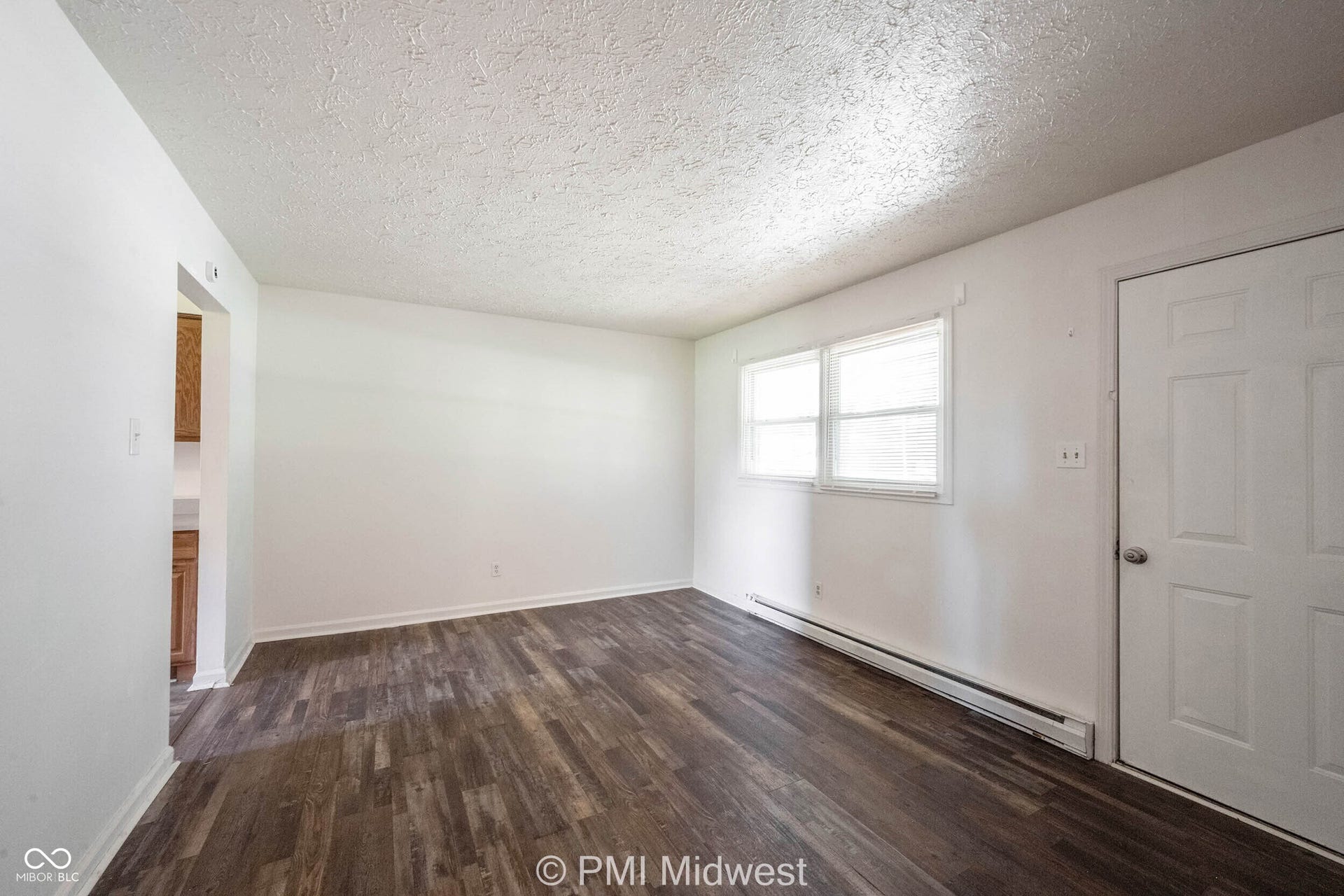 Open living space featuring wood-finish flooring, white walls, and bright natural light from dual windows