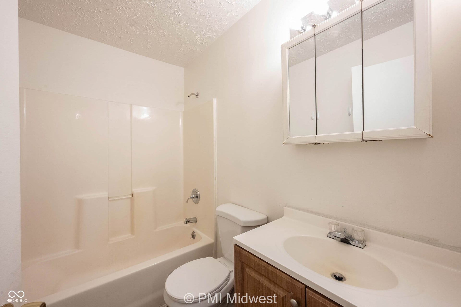 Bathroom featuring a bathtub with an integrated shower, a white toilet, a wood-finish vanity with an integrated sink, a chrome faucet, and a mirrored medicine cabinet