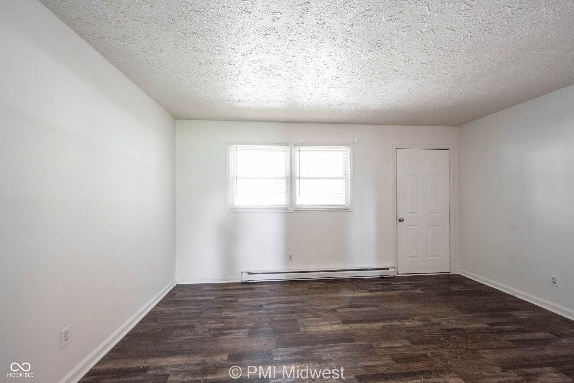 Spacious room featuring wood-finish flooring, white walls, and a textured ceiling