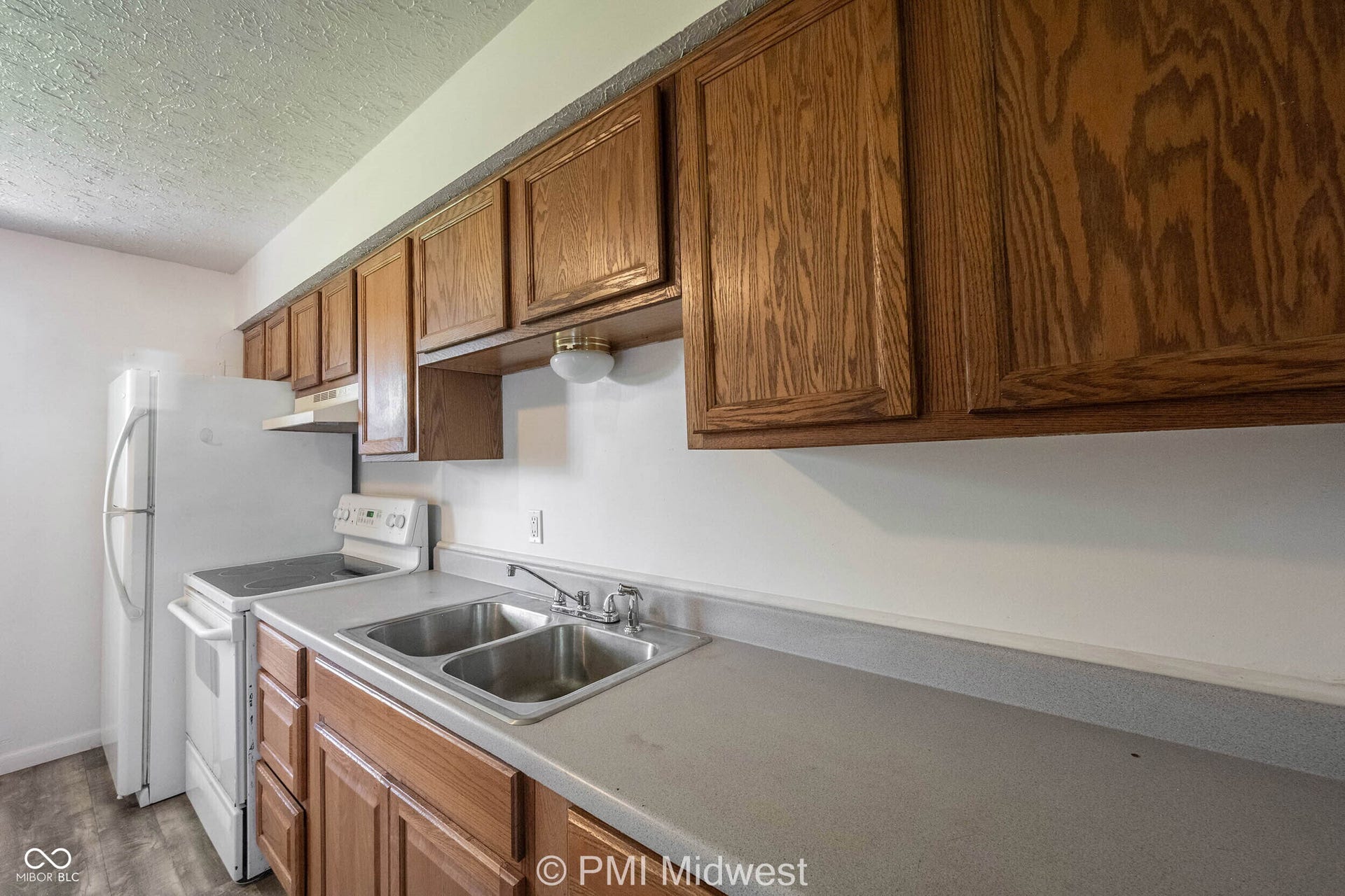 Virtually Altered - Kitchen featuring wood cabinetry, a double basin stainless steel sink, and white appliances including a refrigerator and electric range