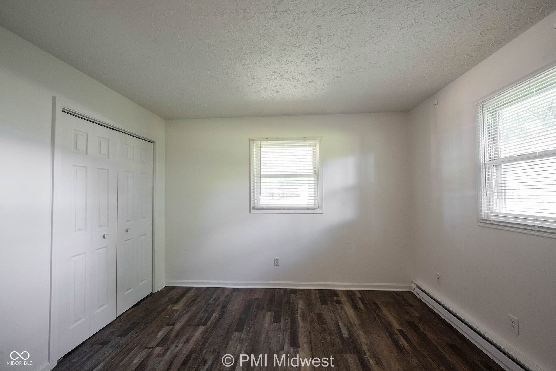 Room featuring wood-finish flooring, white walls, and two windows with horizontal blinds