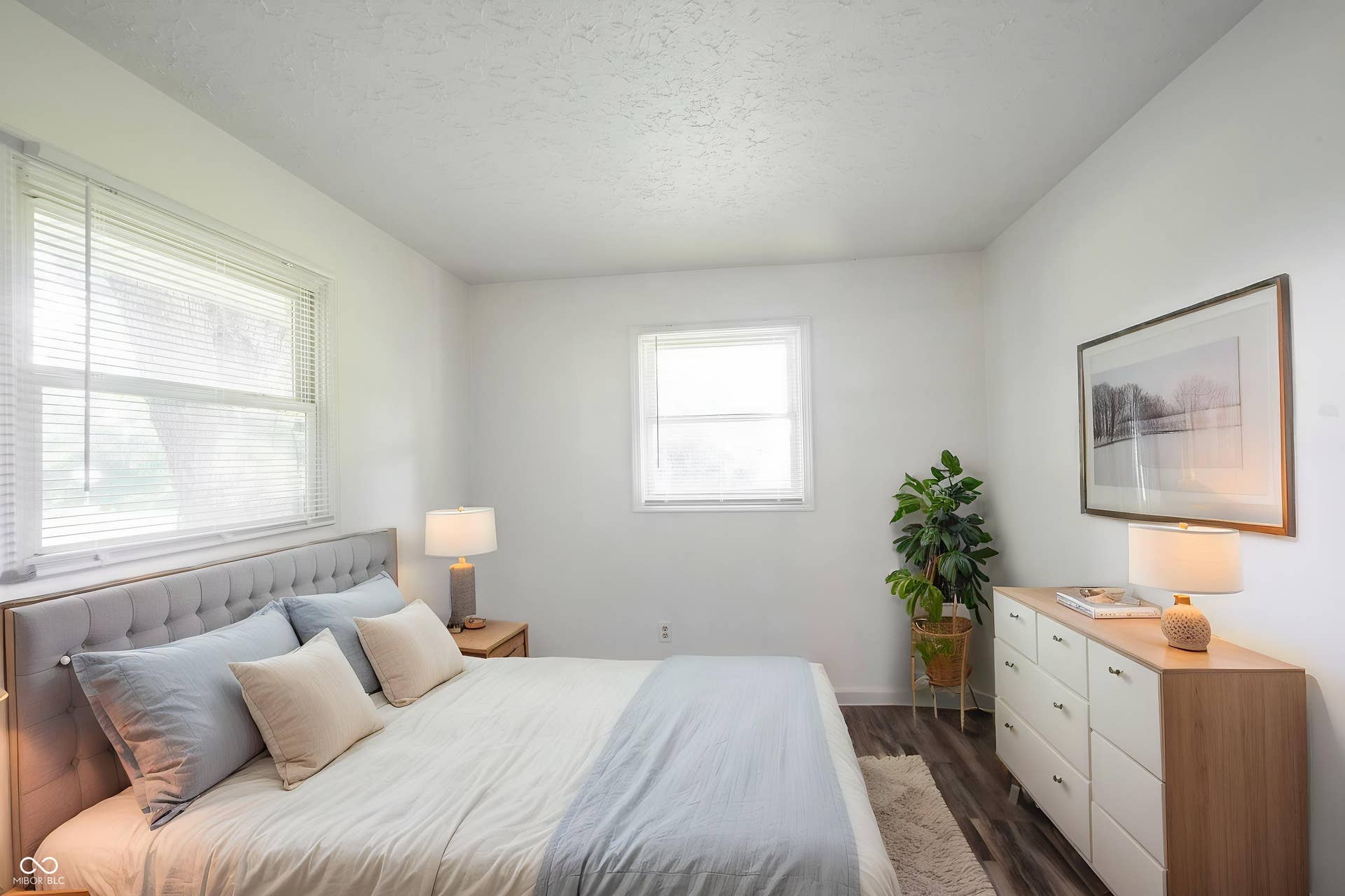 Virtually Altered - Bedroom featuring two windows with blinds, wood-finish flooring, and white walls