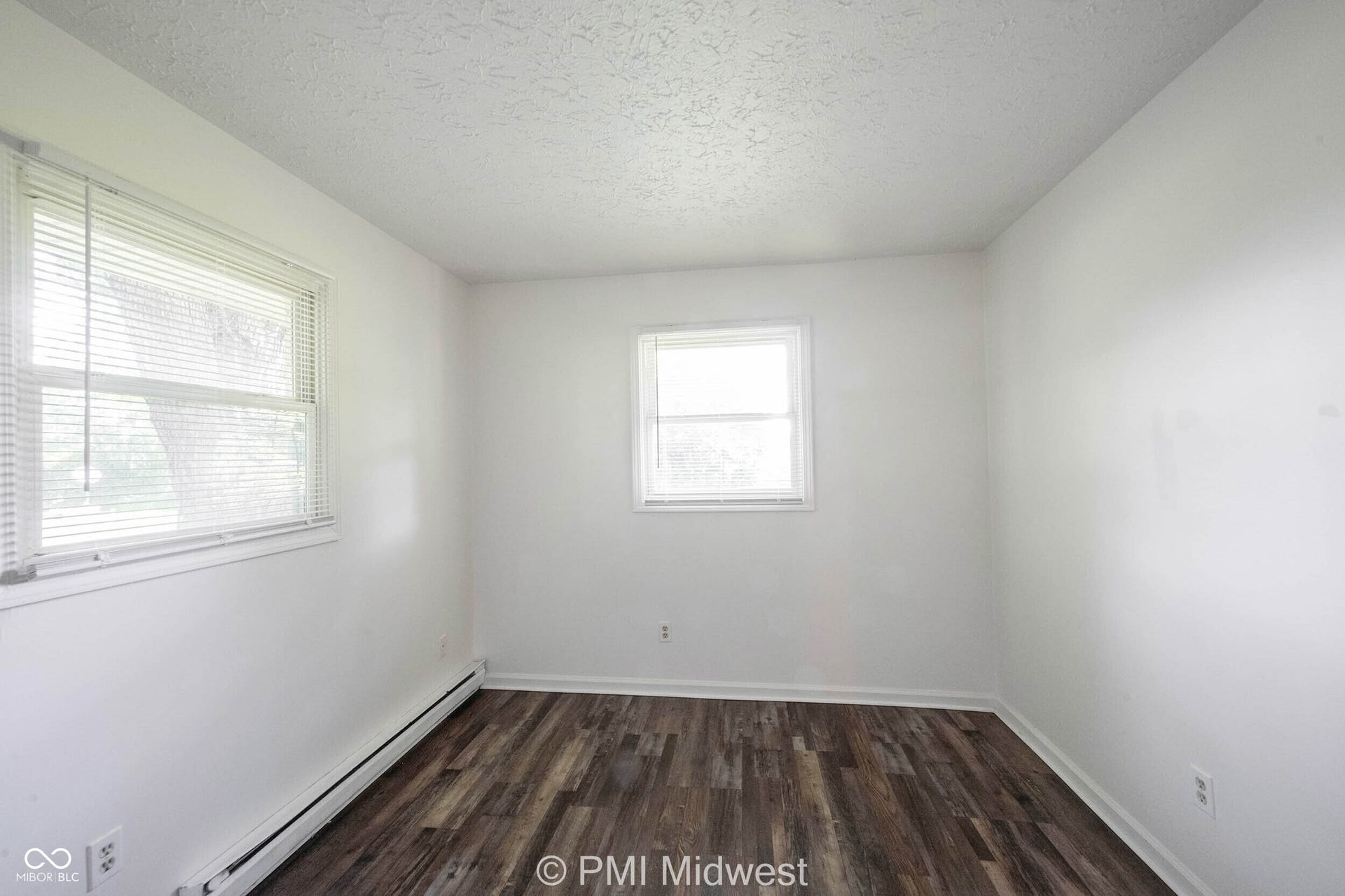 Room featuring wood-finish flooring, white walls, and two windows with blinds