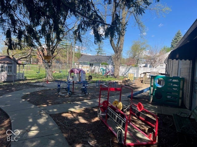 Paved pathway within a large fenced in outdoor backyard area, includes play equipment, and wood deck!