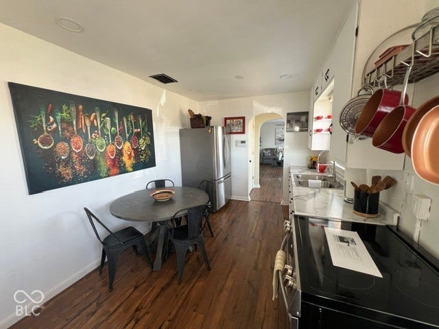 Laminate flooring, recessed lighting, white cabinetry, stainless steel refrigerator, and a built-in range