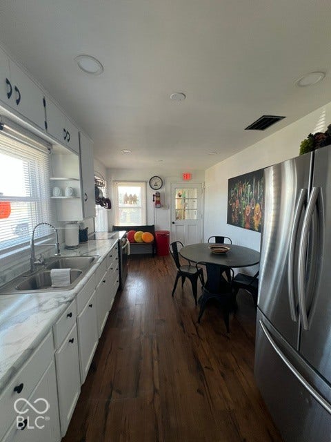 Sleek white cabinetry with black hardware, polished countertop with integrated sink, stainless steel refrigerator, laminate flooring, and recessed ceiling lighting