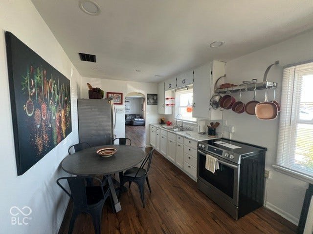 Well-appointed kitchen featuring laminate flooring, white cabinetry, a stainless steel electric range, and a pot rack