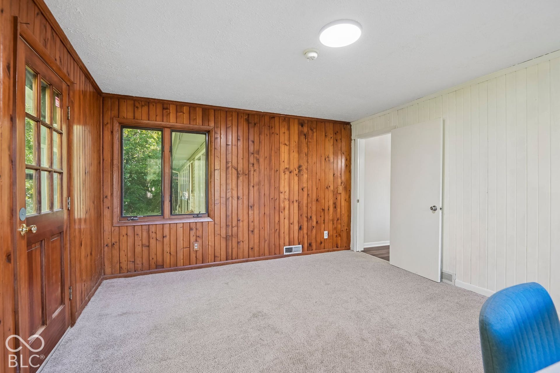 Carpeted flooring, wood paneling, white vertical paneling, and an interior door with a paneled design