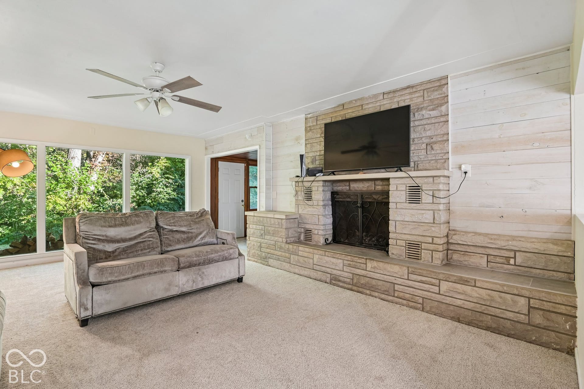 Expansive window wall, stone-front fireplace, integrated mantel, and ceiling fan with lighting