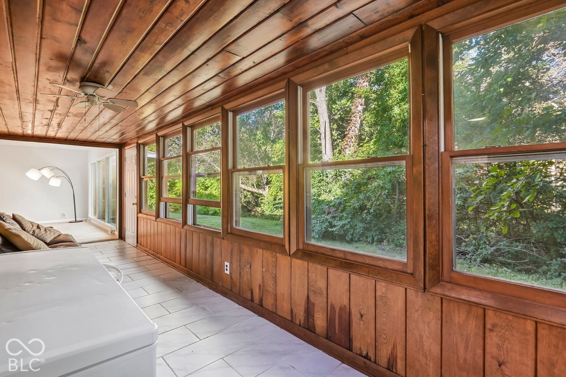 Wood-paneled walls and ceiling, multiple large windows, ceiling fan, and white tile flooring