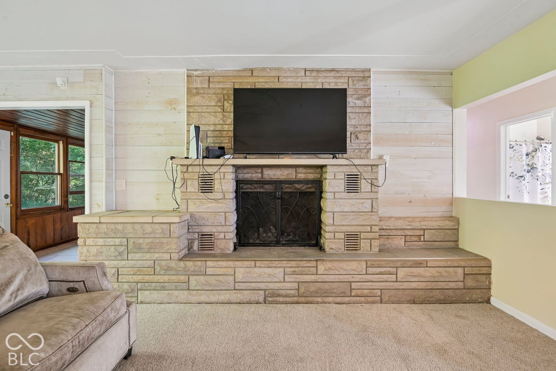 Stone-faced fireplace with a hearth extension, wall-mounted display, and carpeted flooring