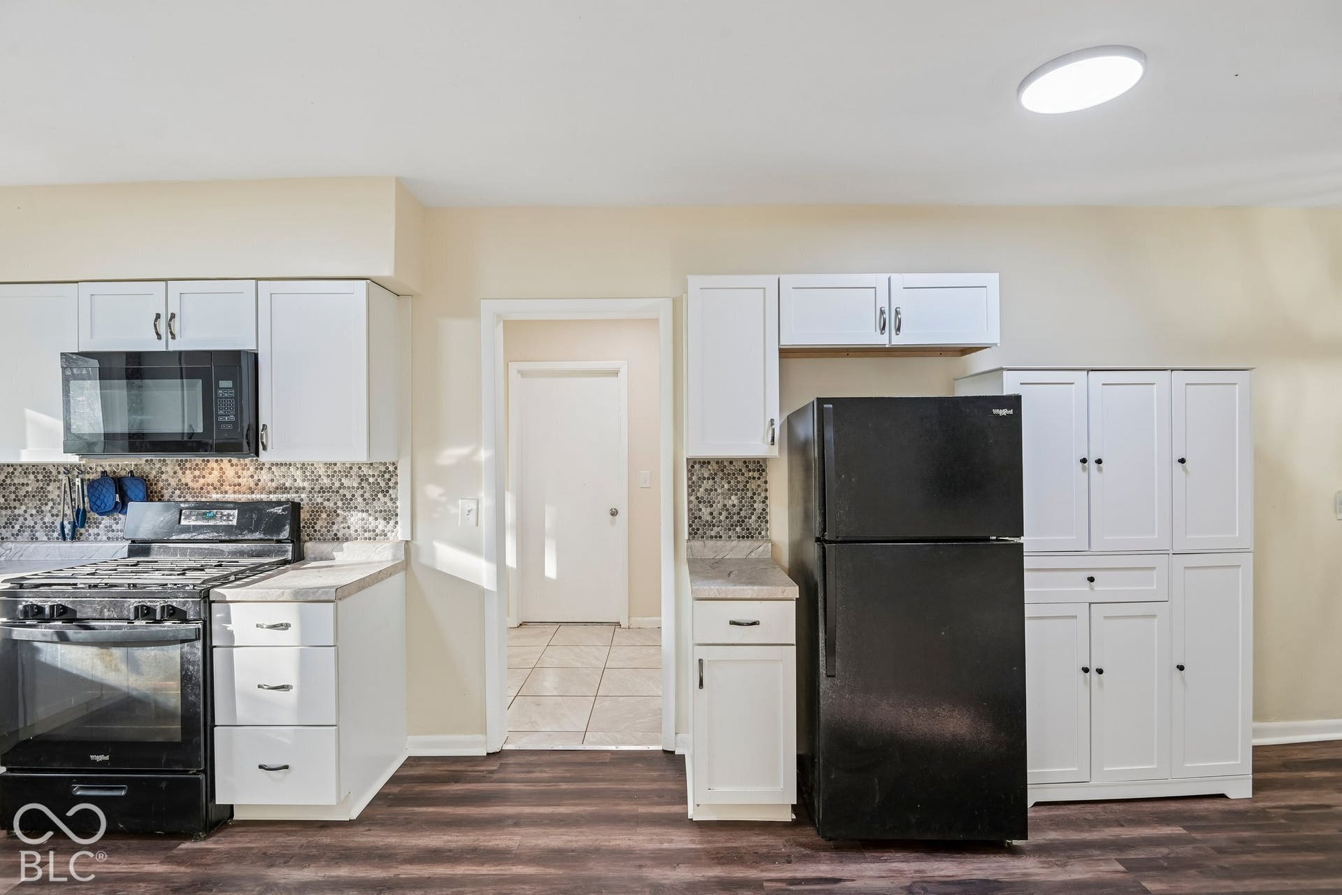 White cabinetry, built-in microwave, wood-finish flooring, and a tile backsplash