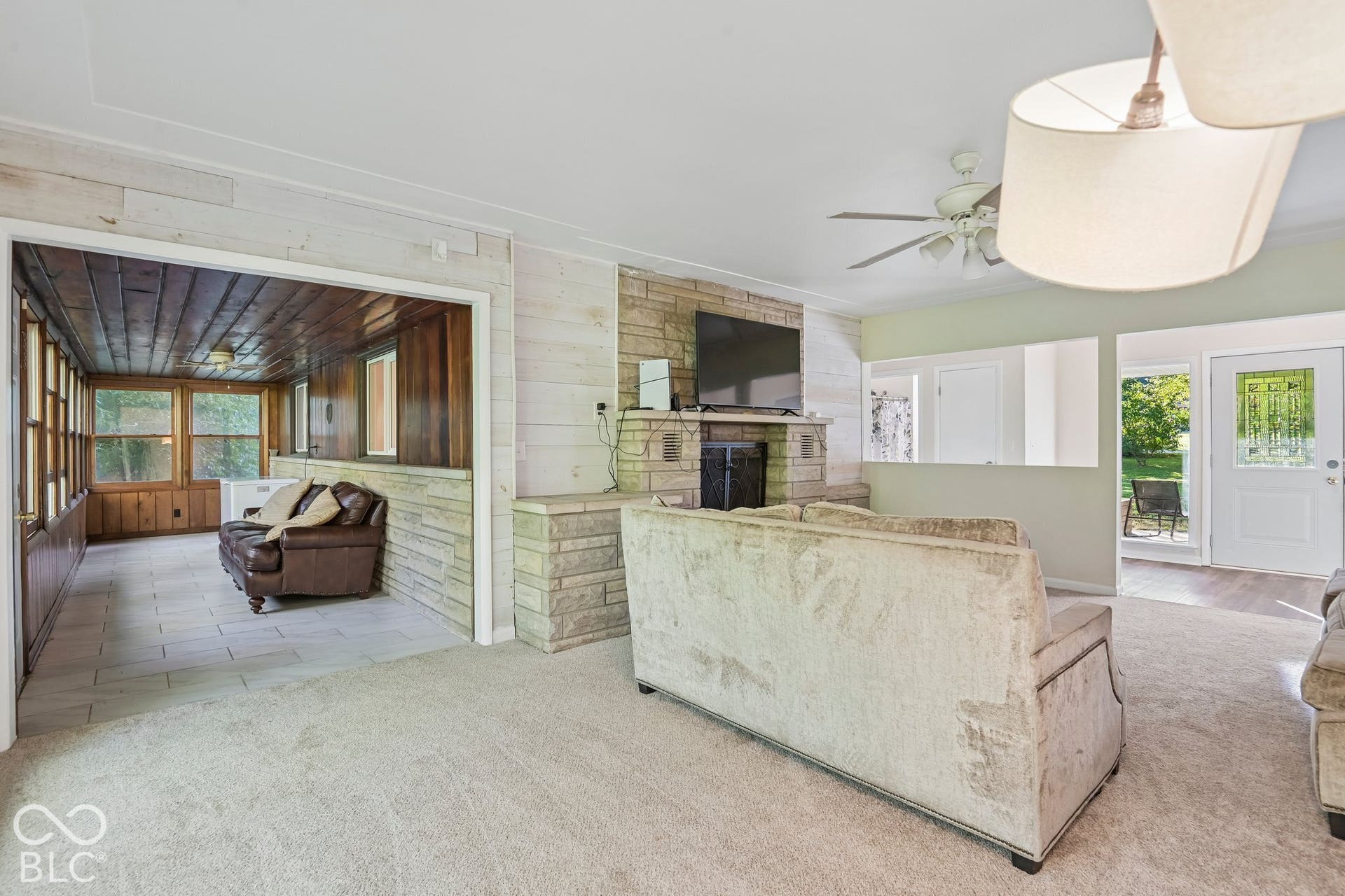 Stone-clad fireplace with mantel, ceiling fan with integrated lighting, recessed lighting, sunroom with tiled flooring, and wood-paneled walls