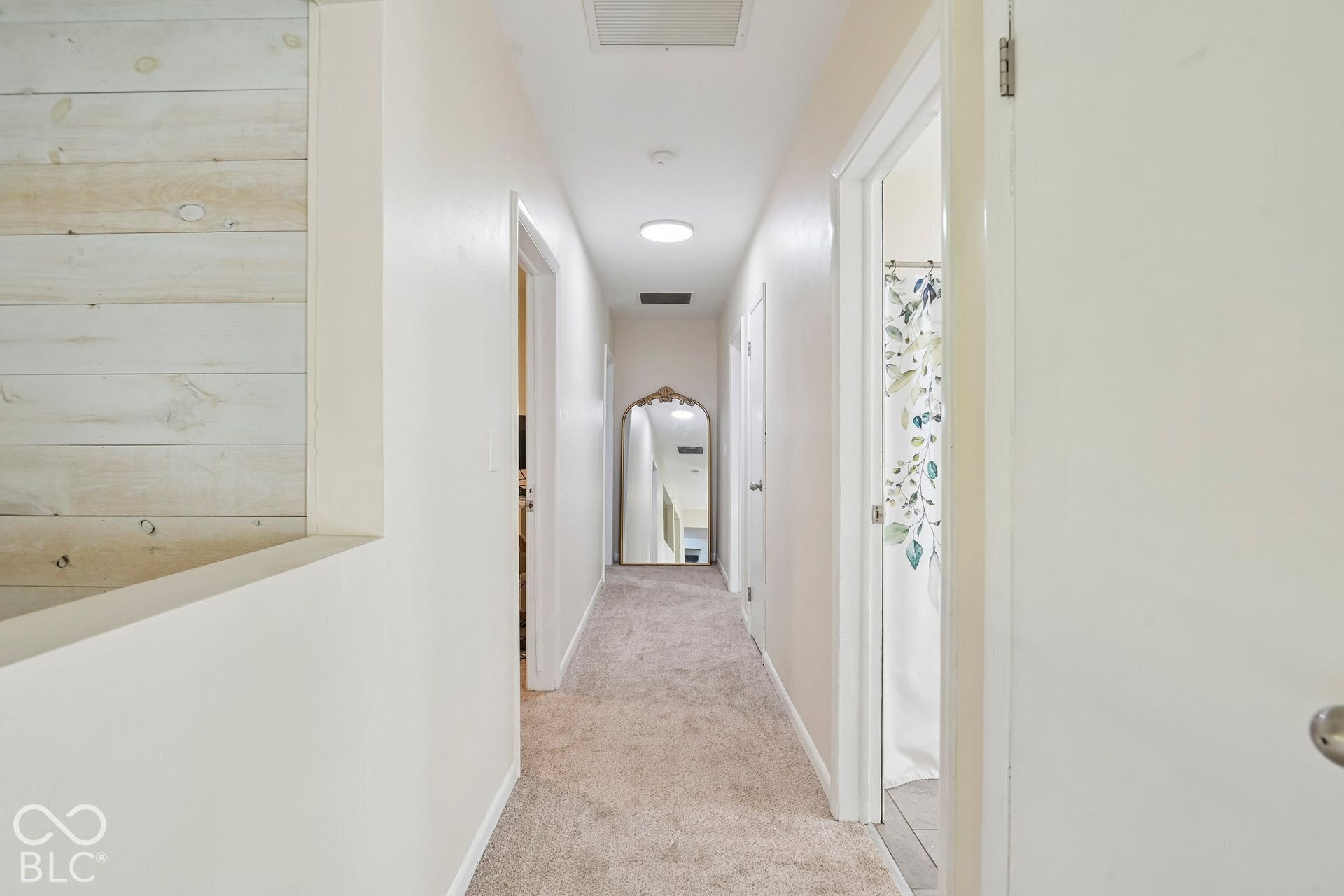 Carpeted hallway featuring a ceiling light fixture, white interior doors, and a wood-paneled partial wall