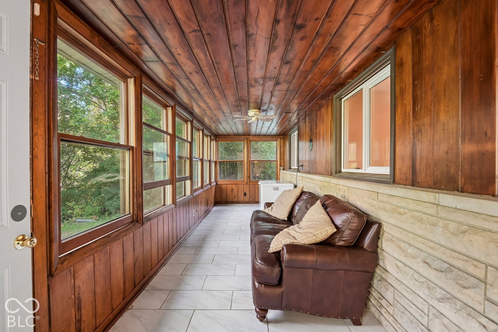 Wood-paneled sunroom featuring a wood-plank ceiling, multiple windows, and tile flooring