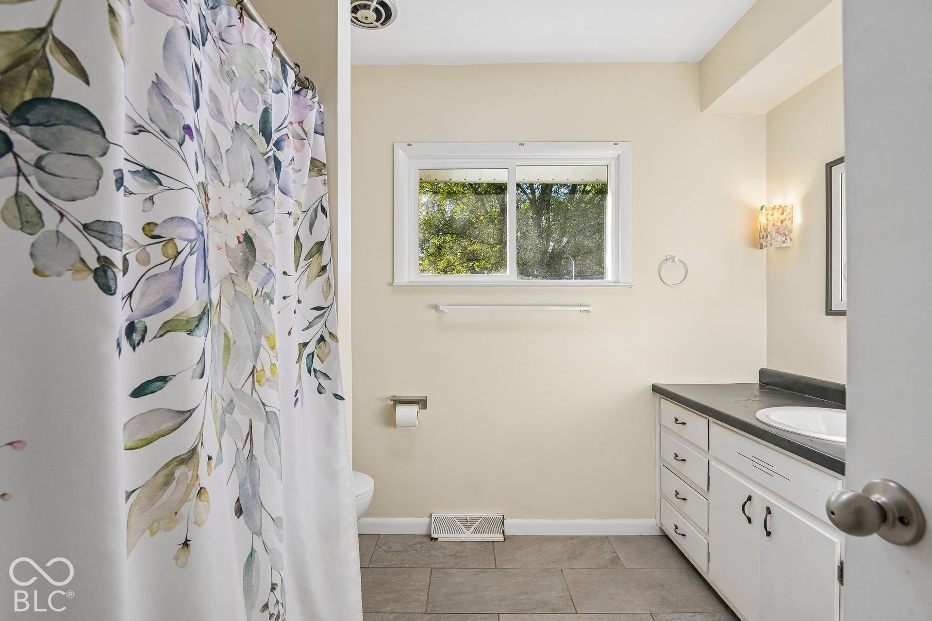 Bathroom featuring a single-pane window, white vanity with cabinet storage, integrated sink, dark countertop, and tiled flooring
