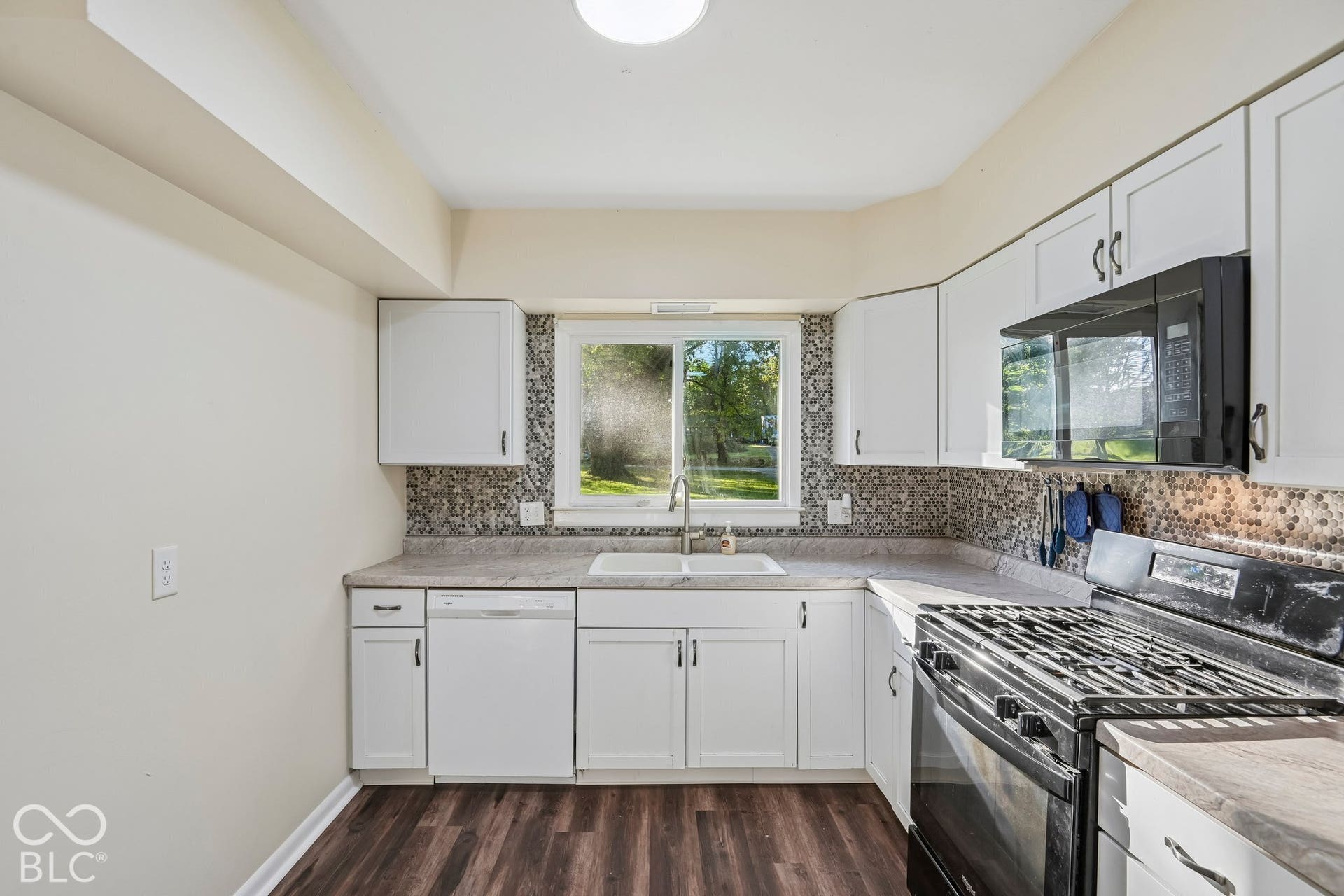 Kitchen featuring white cabinetry, dark wood-finish flooring, a mosaic tile backsplash, a stainless steel sink, and a built-in microwave