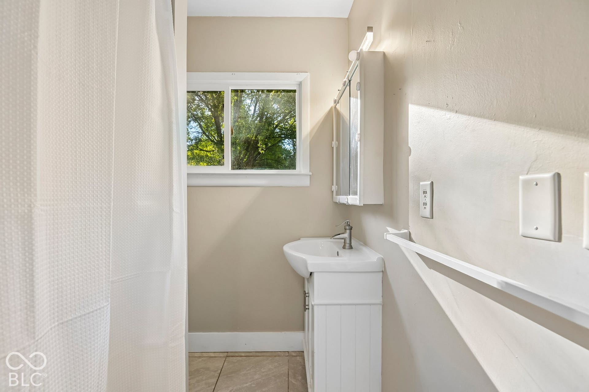 White single-pane window, wall-mounted medicine cabinet with mirrored door, pedestal sink with cabinet, and tiled flooring