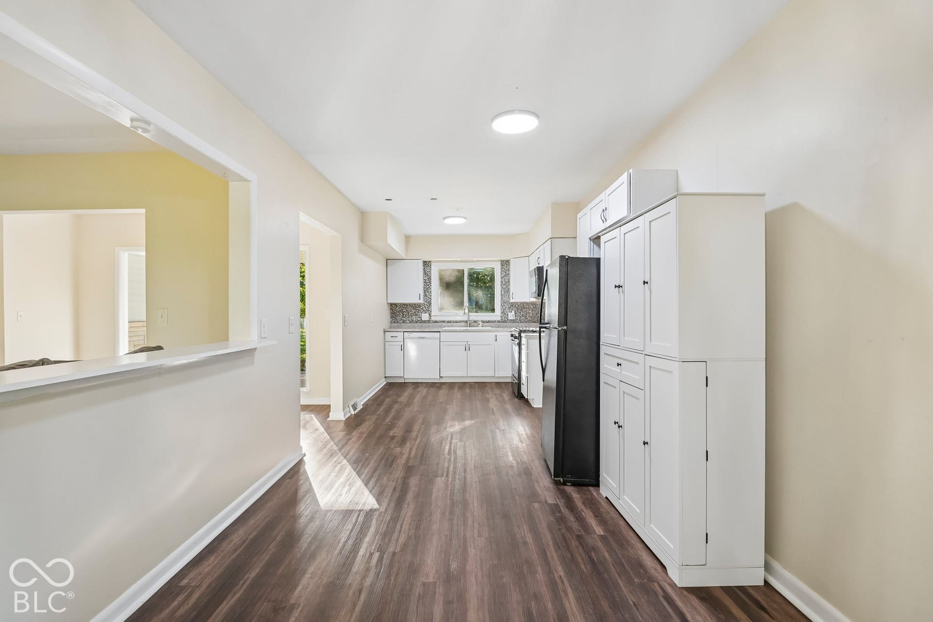 Galley kitchen featuring white cabinetry, stainless steel appliances, wood-finish flooring, recessed ceiling lighting, and ample counter workspace with a pass-through window to the adjoining room