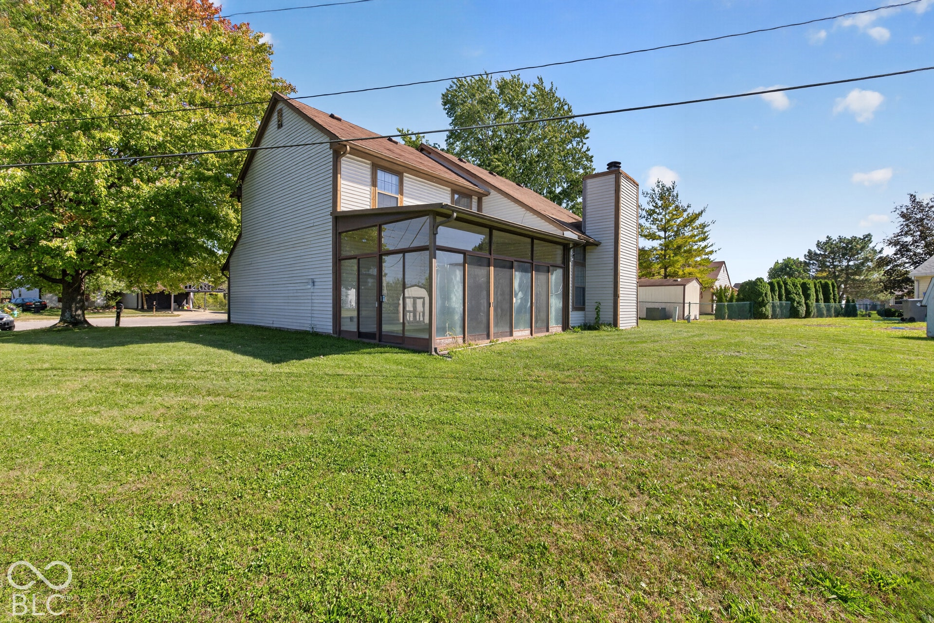 Expansive grassy yard area with a sunroom addition and a prominent exterior chimney