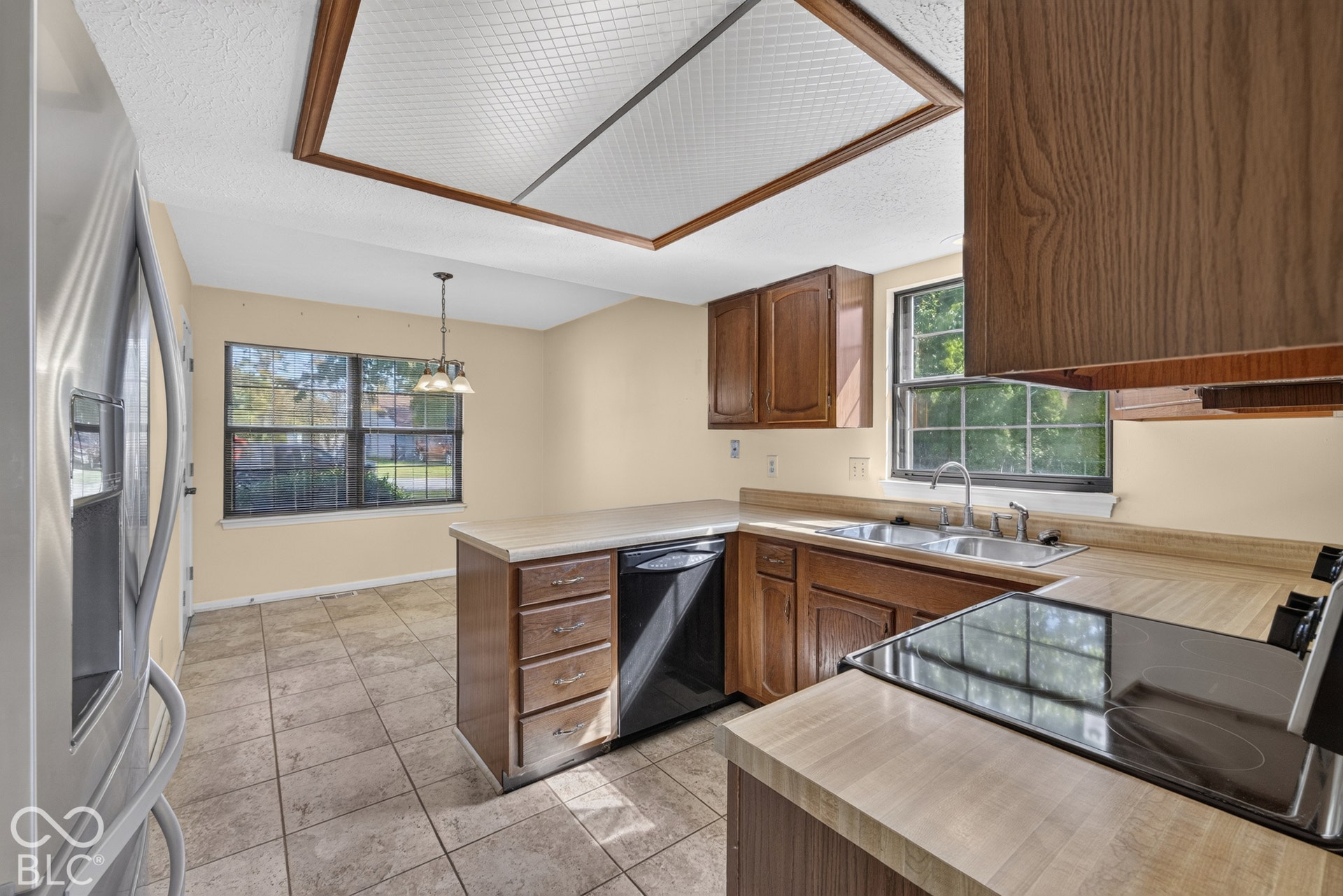 Kitchen featuring wood-finish cabinetry, tile flooring, L-shaped countertops, a double basin sink, and a built-in electric range