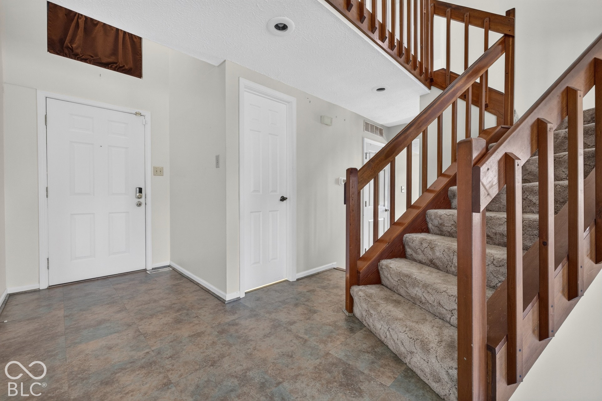 Entryway featuring durable flooring, a paneled entry door with smart lock hardware, a secondary paneled door, and a staircase with wood railings and carpeted treads