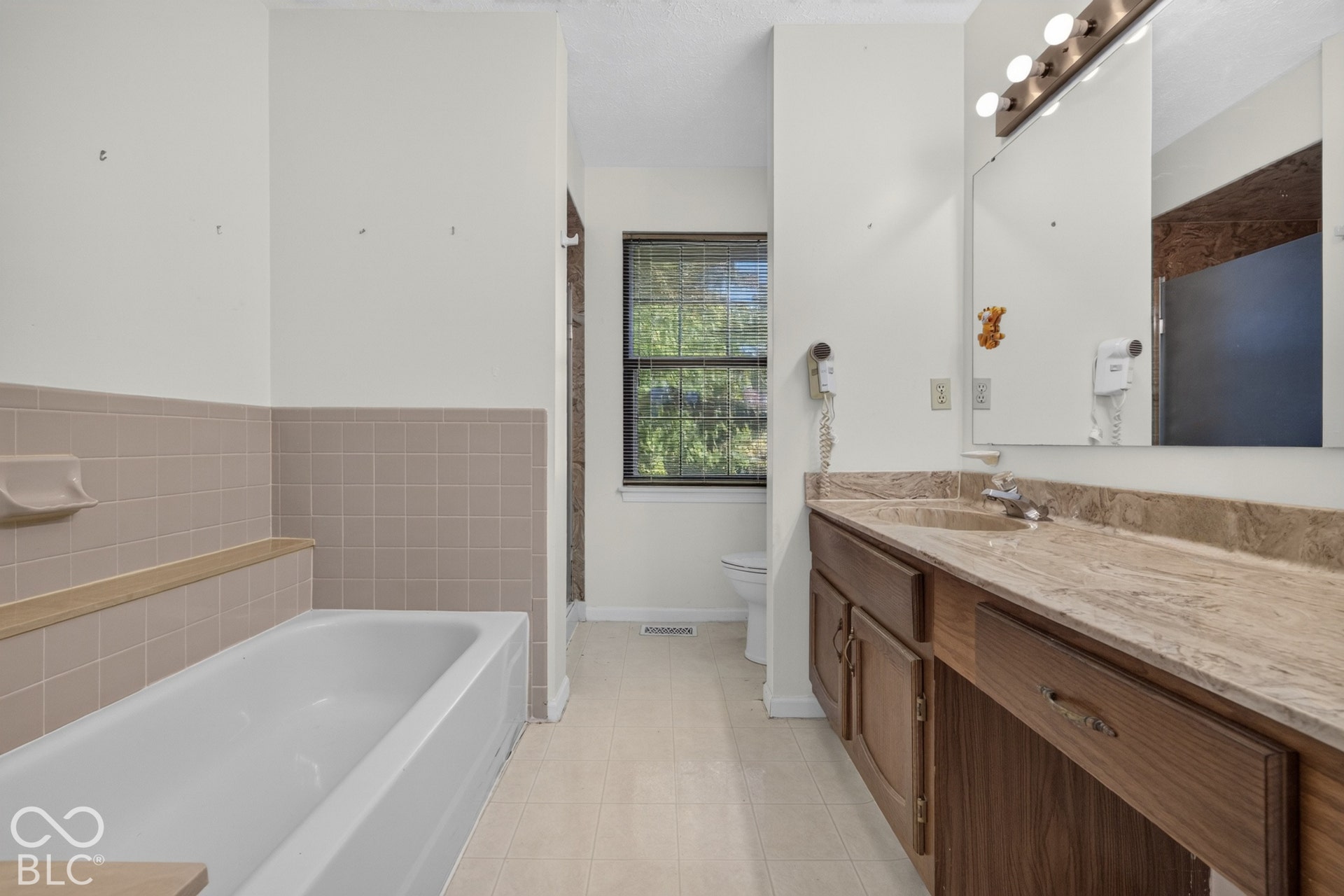 Double vanity with a large mirror, wood-finish cabinetry, and a built-in bathtub with tiled surround