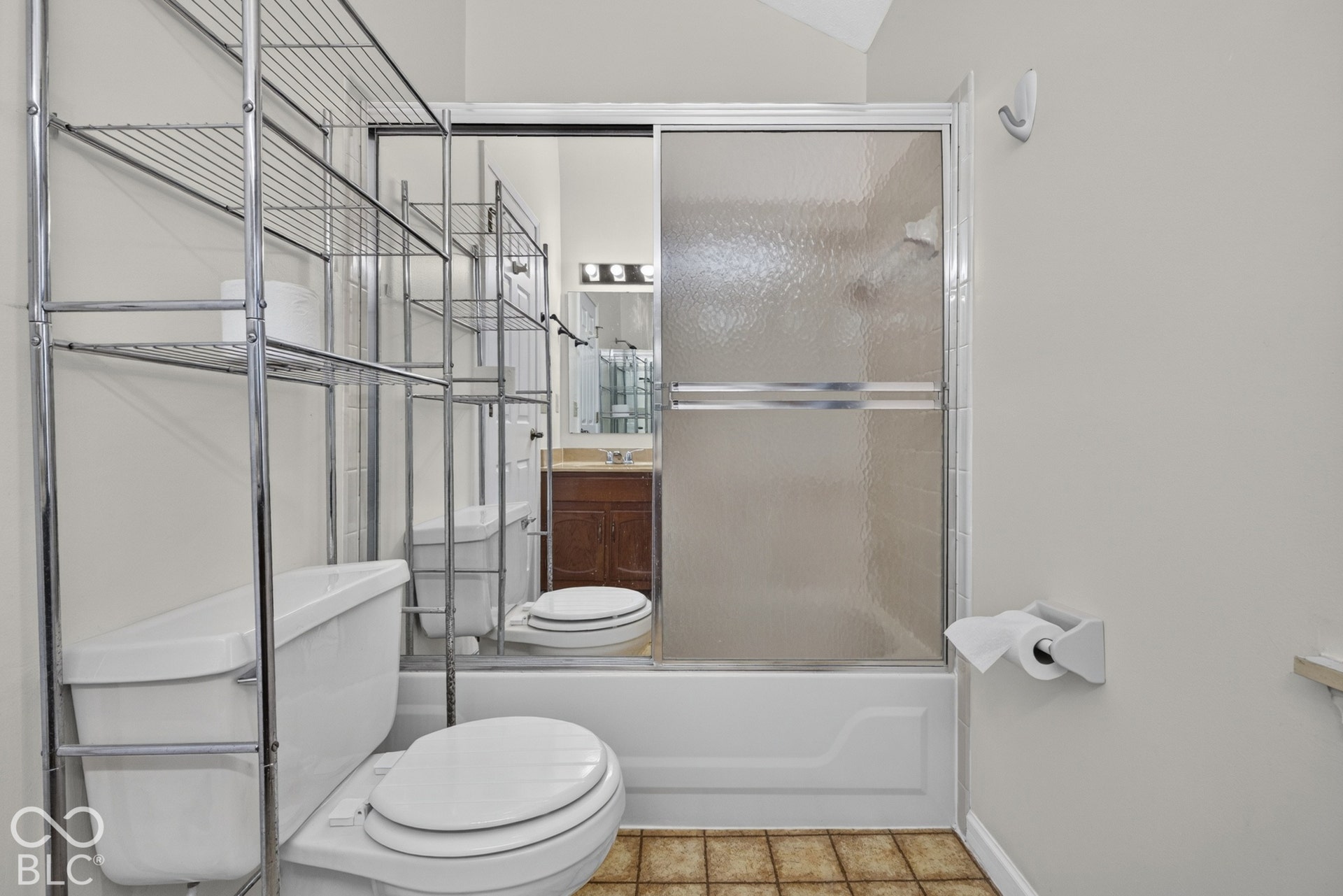 Bathtub with frosted glass sliding doors, ceramic tile flooring, and a mirrored vanity with a light fixture