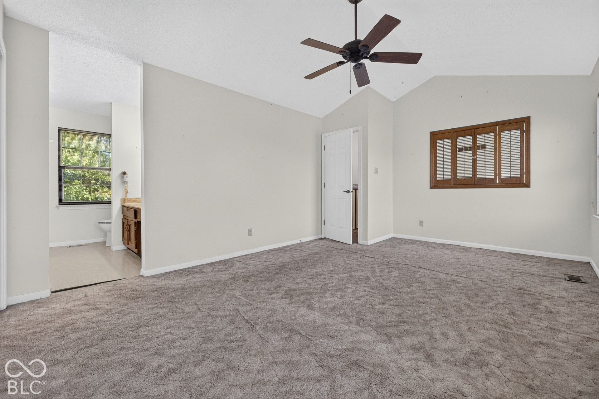 Vaulted ceiling with a ceiling fan, carpeted flooring, and a window with wood shutters