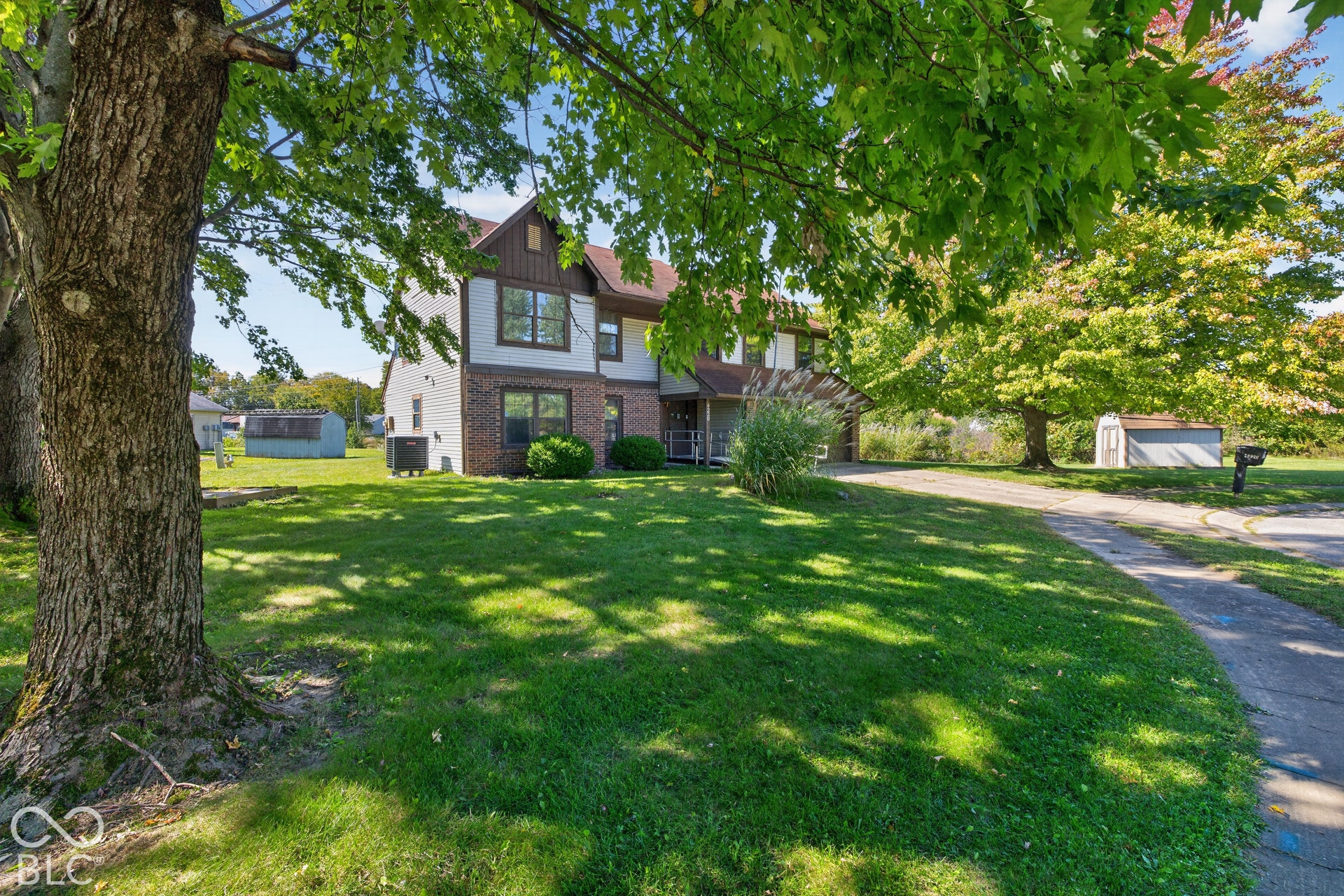 Two-story residence featuring brick and siding facade, mature trees, and a paved driveway