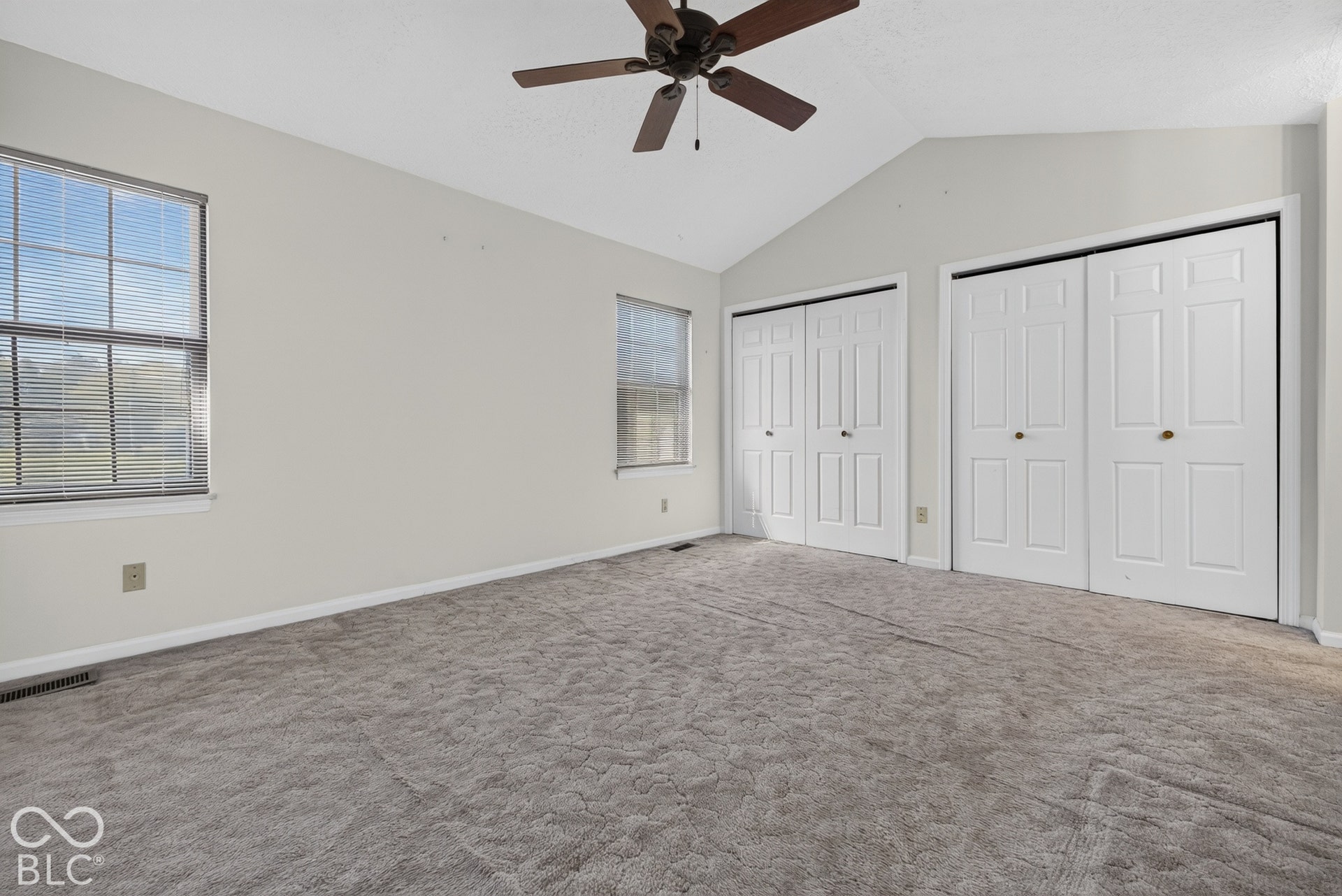 Vaulted ceiling with ceiling fan, two windows with blinds, and two sets of bi-fold closet doors