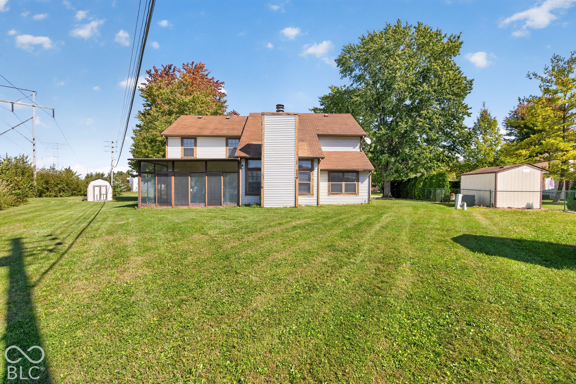 Expansive green lawn with a screened-in porch, multiple windows, and two storage sheds