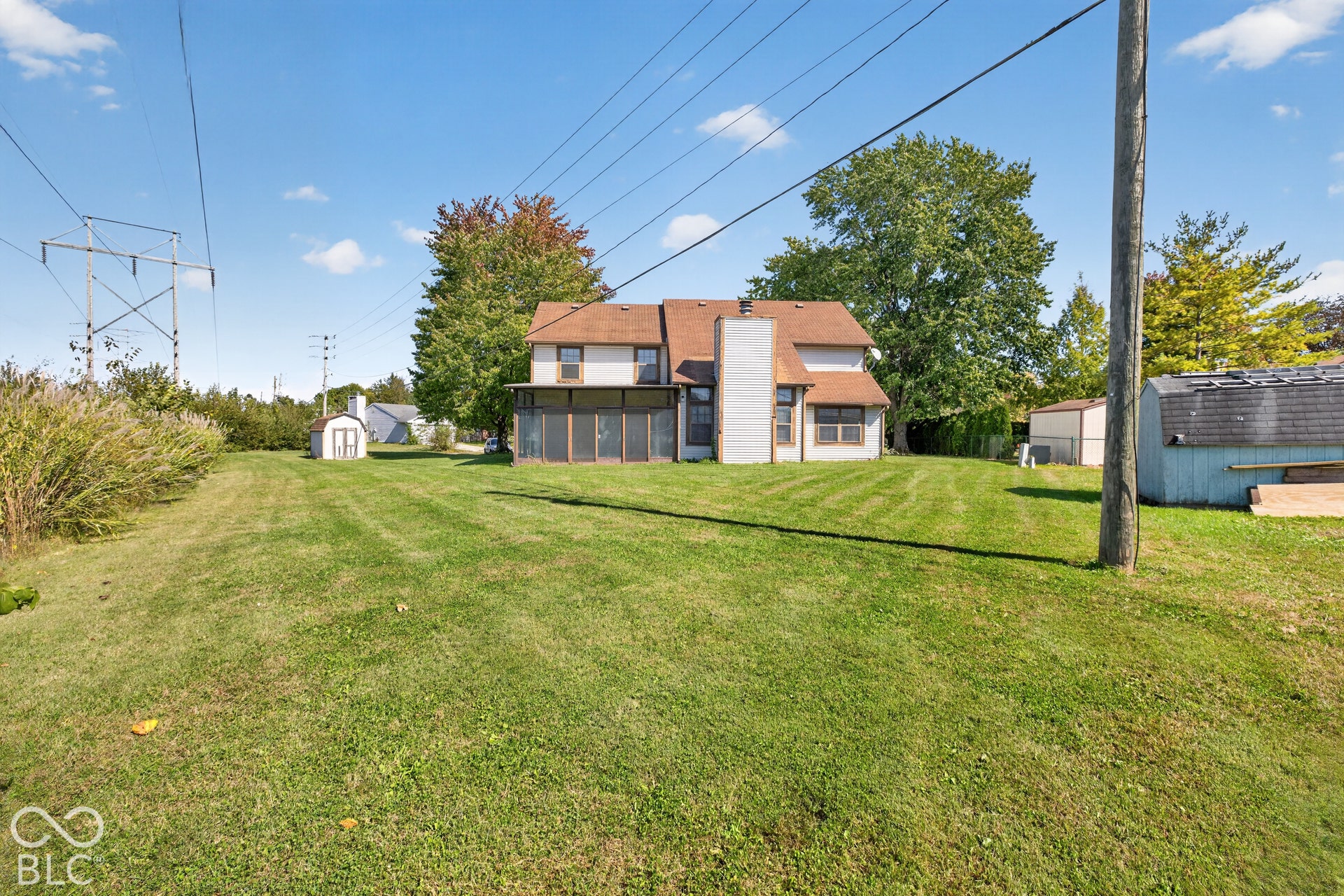 Expansive rear yard featuring a large screened porch, a two-story residence with a gabled roof, and two outbuildings