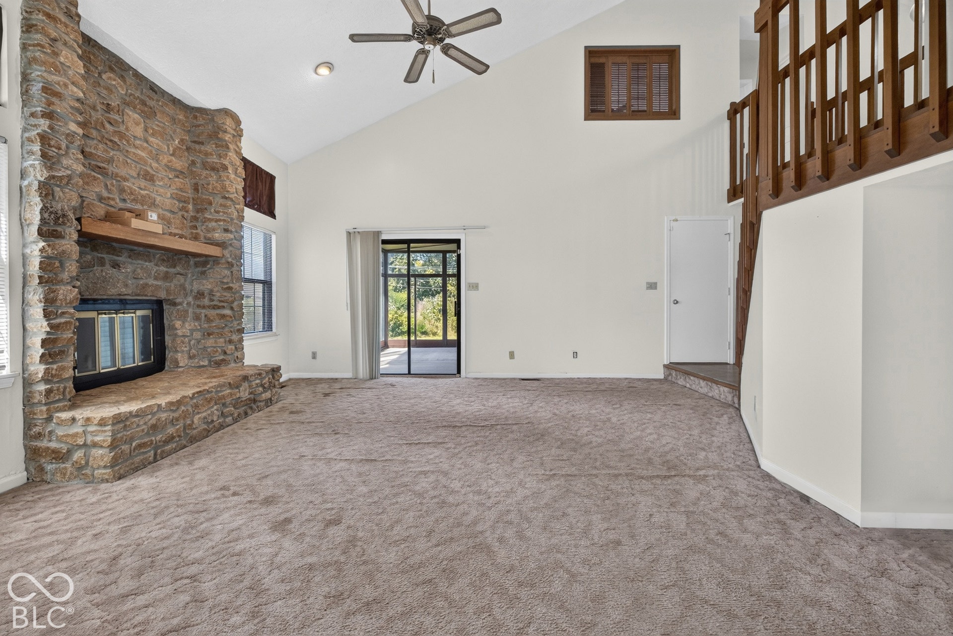 Vaulted ceiling, stone fireplace with hearth, wood mantle, sliding glass door, and exposed wood staircase railing