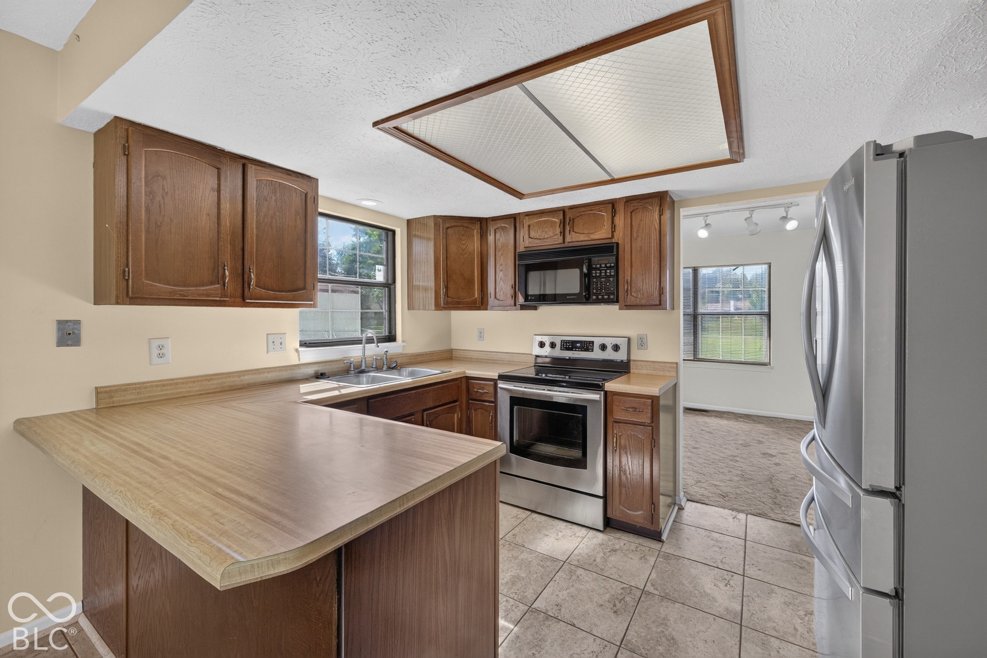 Kitchen featuring wood-finish cabinetry, stainless steel appliances, a corner sink, and tiled flooring