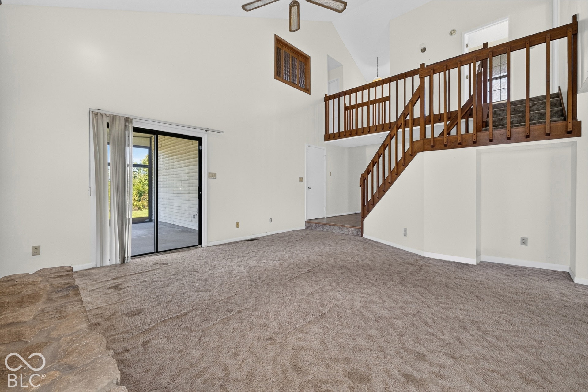 Vaulted ceiling with a ceiling fan, sliding glass door, and a built-in wooden staircase leading to an upper level