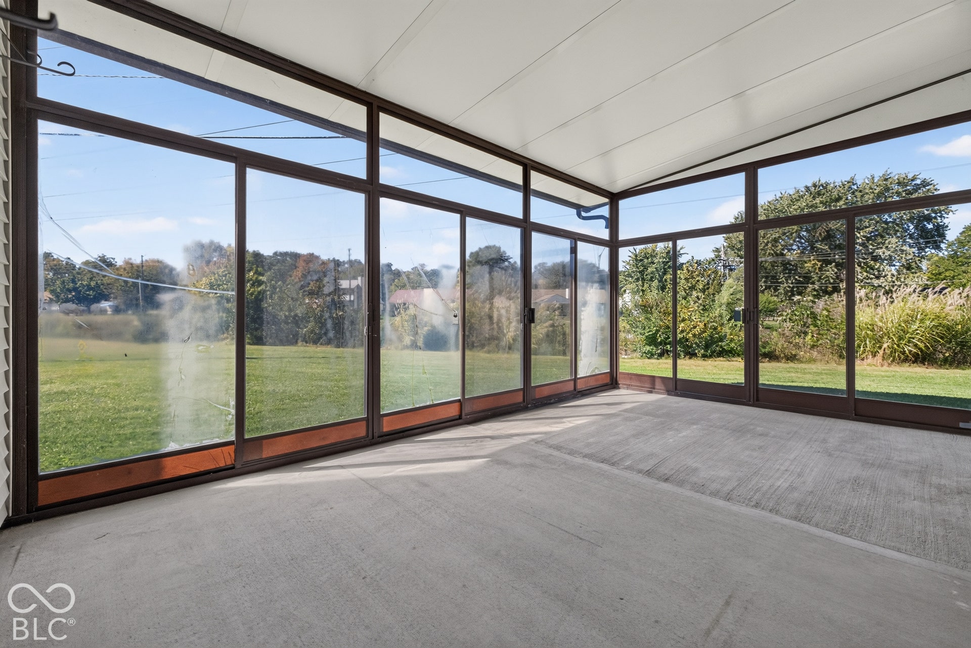 Enclosed patio with full-height glass panels, concrete flooring, and a white paneled ceiling