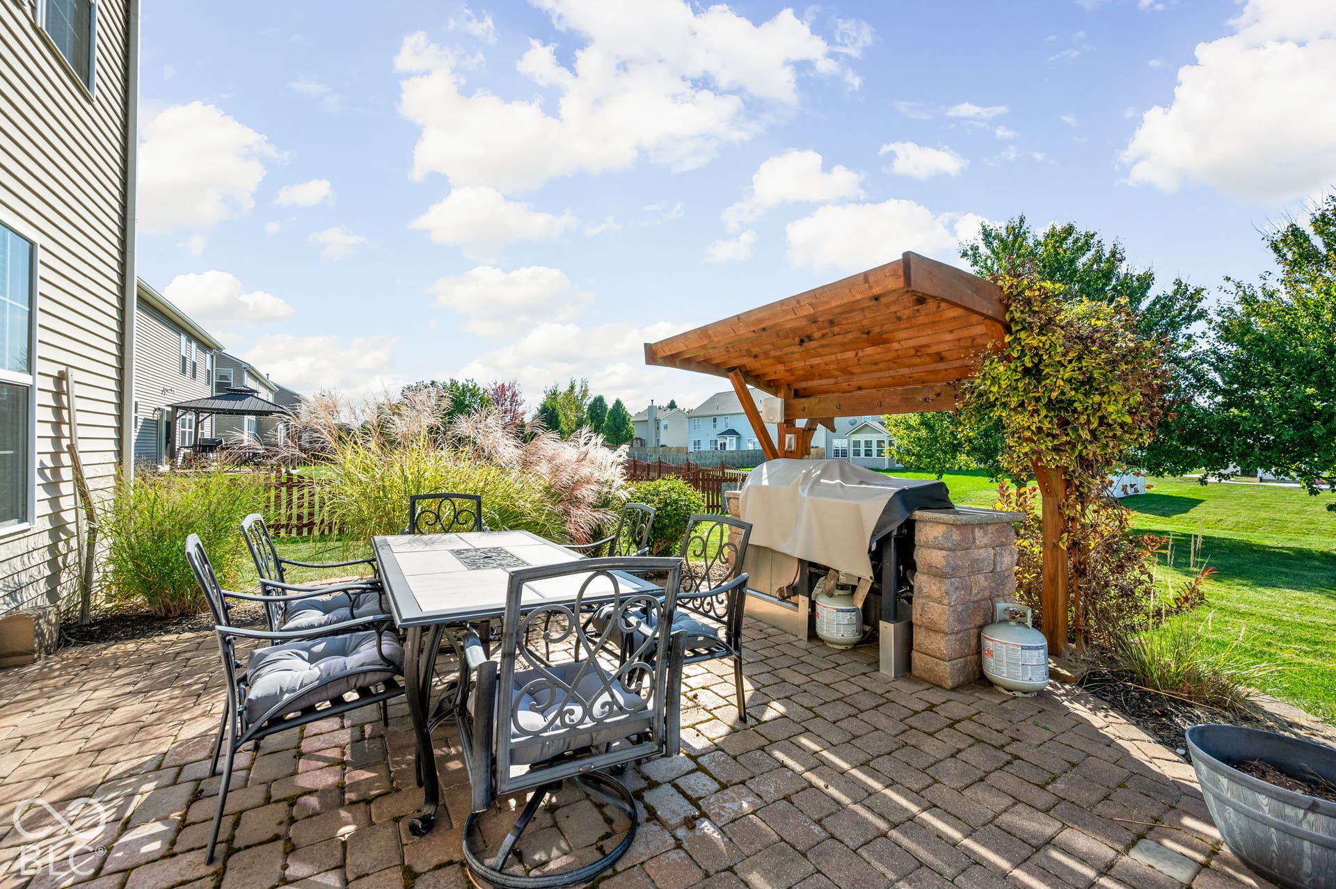 Paver patio featuring a wooden pergola, built-in outdoor kitchen base, and verdant landscaping