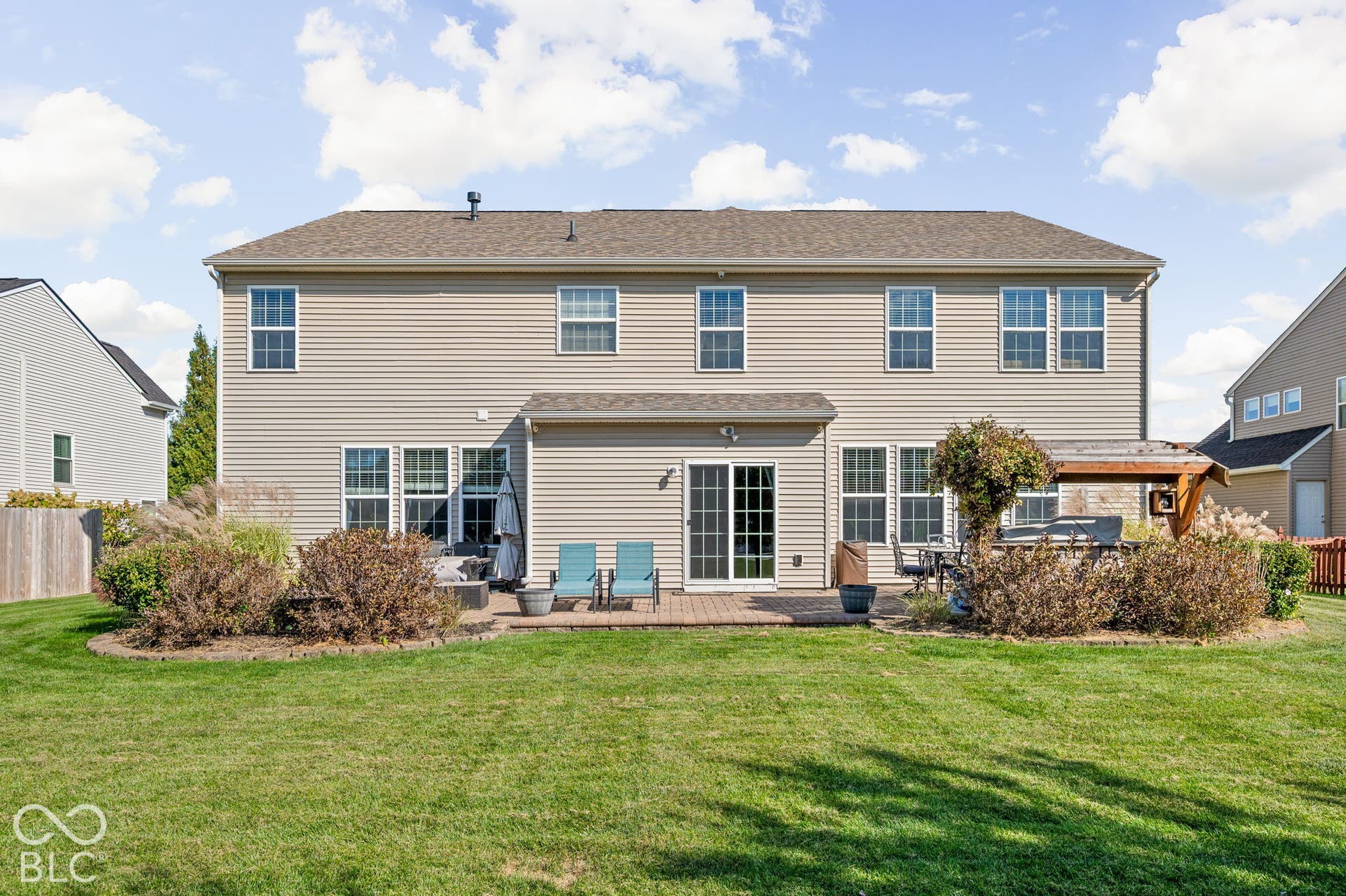 Expansive backyard featuring a manicured lawn, brick paver patio, and mature landscaping